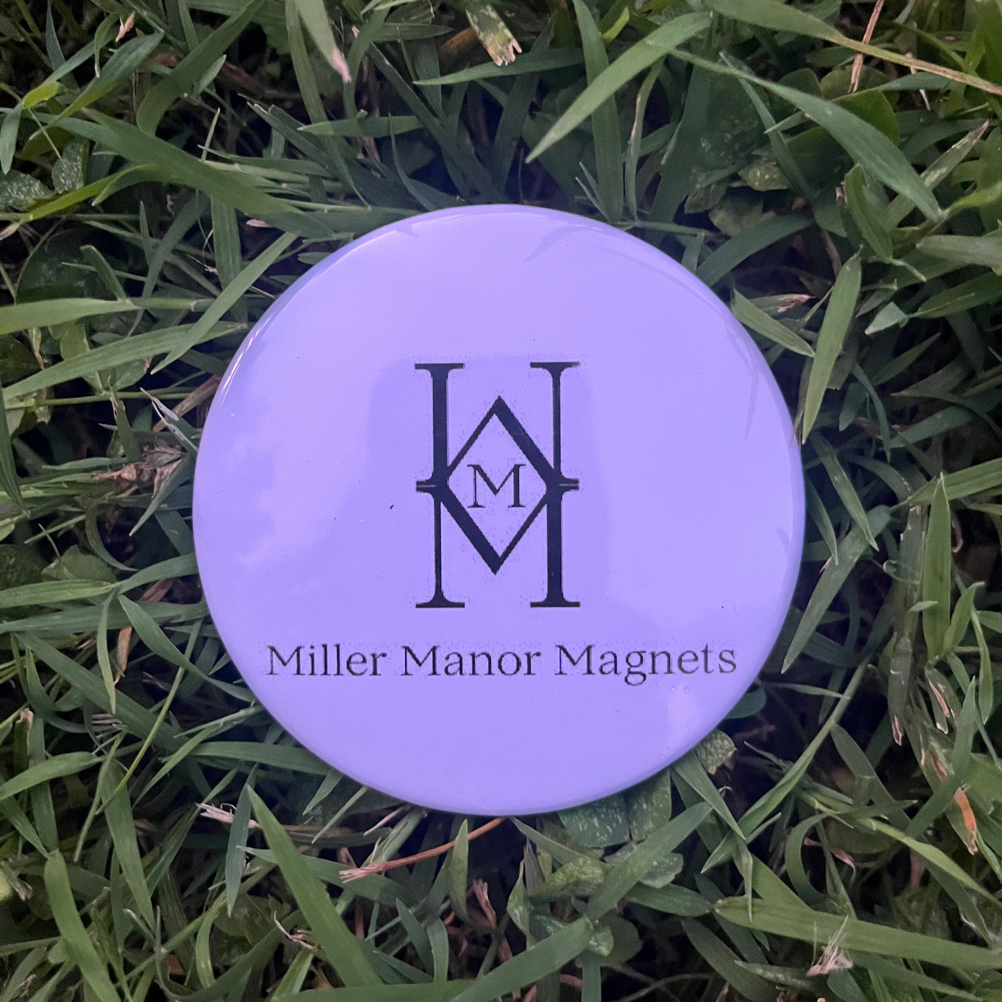 White button with 'Miller Manor Magnets' logo on grass