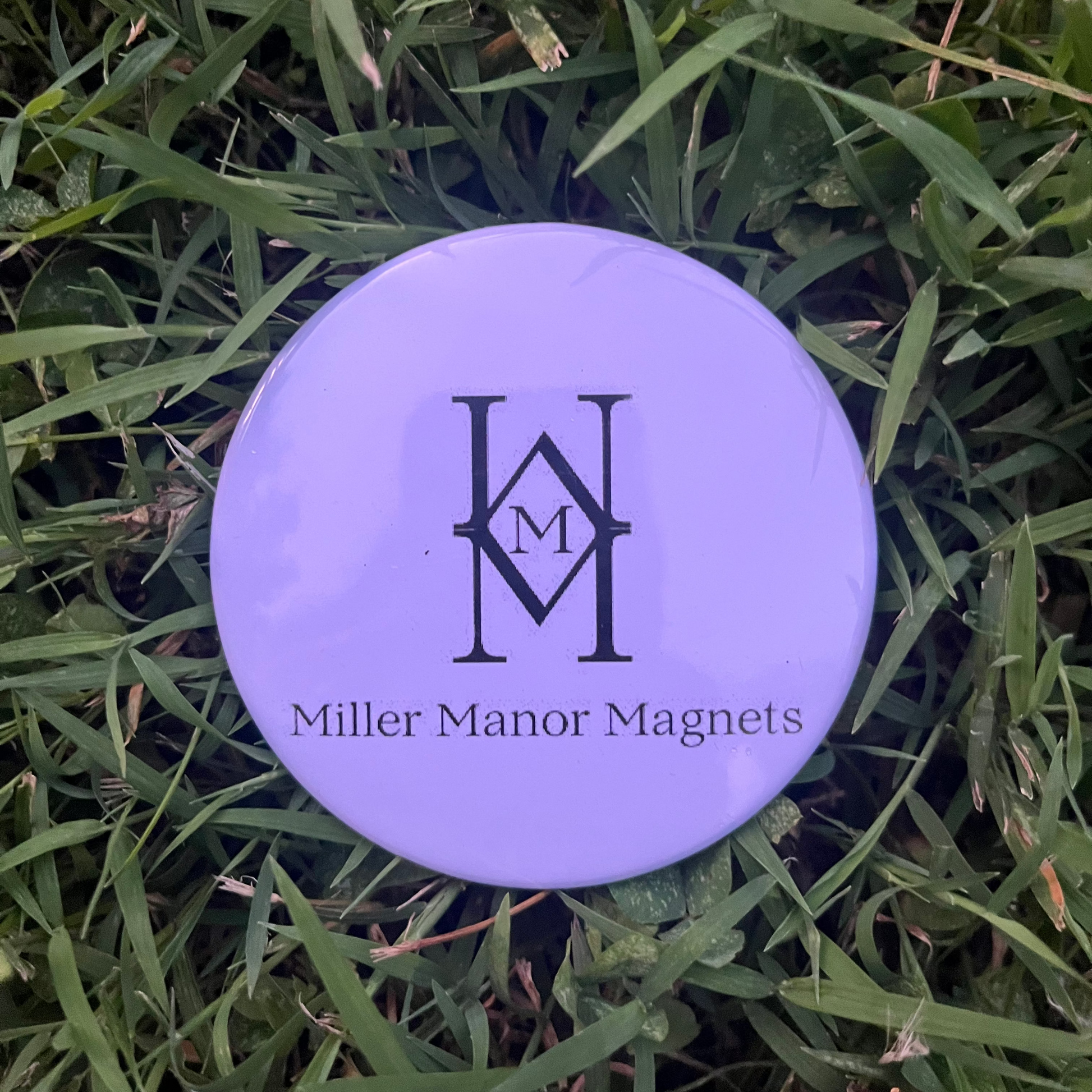 White button with 'Miller Manor Magnets' logo on grass