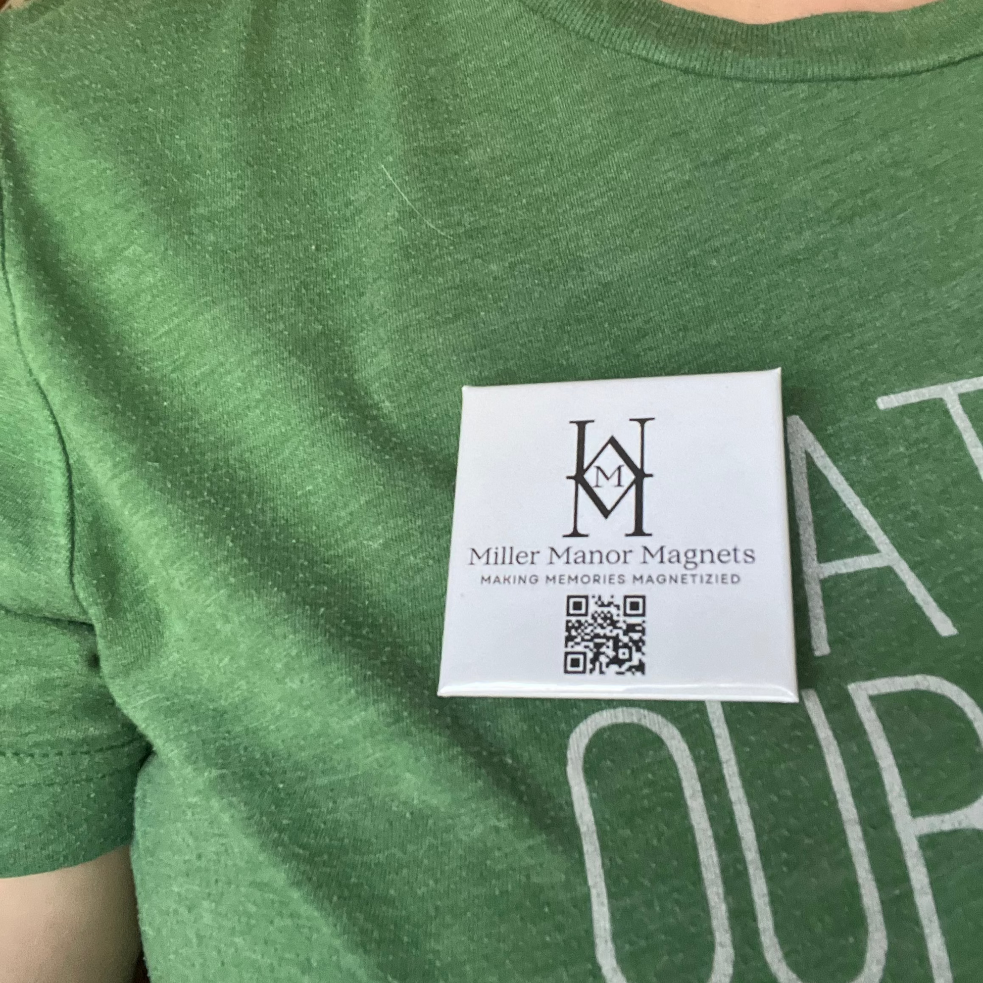 Green t-shirt with a white pin featuring a logo 